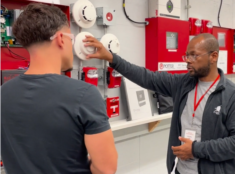 Fire Tech instructor, Shawn Lee, talks with a student in front of a Fire Alarm test set-up.