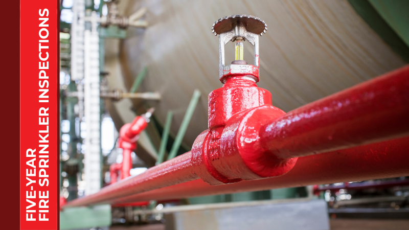 A fire sprinkler affixed to a bright red pipe in an industrial setting.