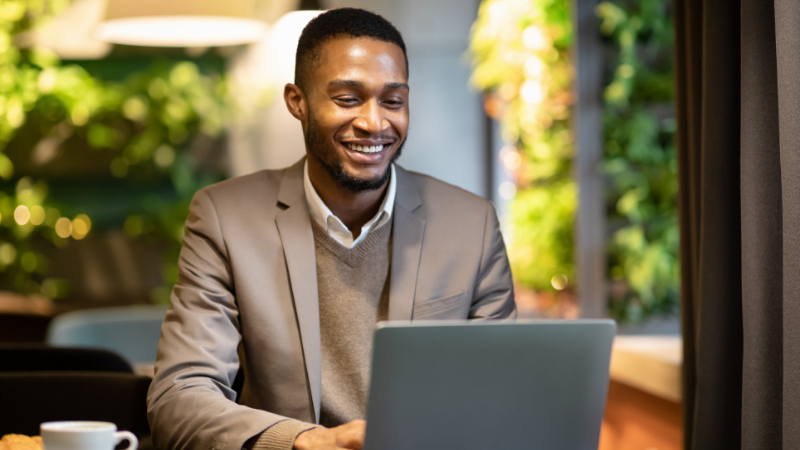 A young professional wearing a blazer sits in an office on his laptop.